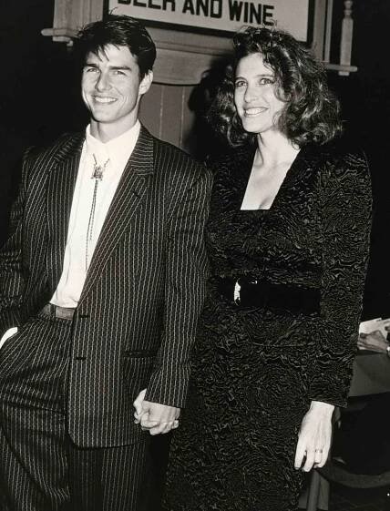 Tom Cruise in a pinstriped suit and Mimi Rogers in a textured, belted dress holding hands