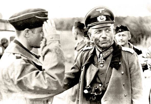 A black and white photo of General Heinz Guderian in military uniform with medals and cap being saluted by a soldier.