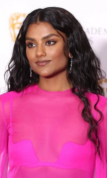 Simone Ashley wearing a hot pink dress with her long, thick hair parted in the middle