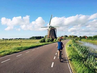 Young woman in shorts riding a bike near traditional Dutch windmill near Maasland, Holland, Netherlands