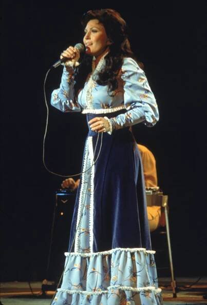 Circa 1980, American country singer and songwriter Loretta Lynn performs on stage, wearing a long dress.
