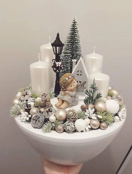 a person holding up a white christmas centerpiece with candles and ornaments on top of it