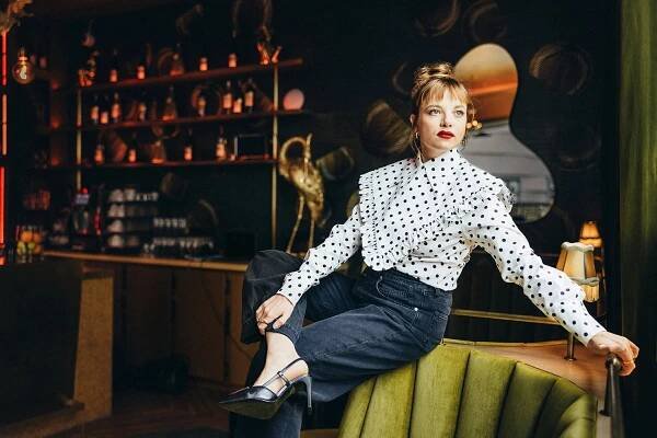 Jella Haase sitzt auf der Lehne eines grünen Sofas, im Hintergrund eine Bar