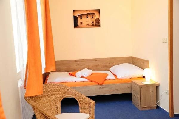a small room with a bed with an orange curtain at Hotel Praha Potštejn in Potštejn