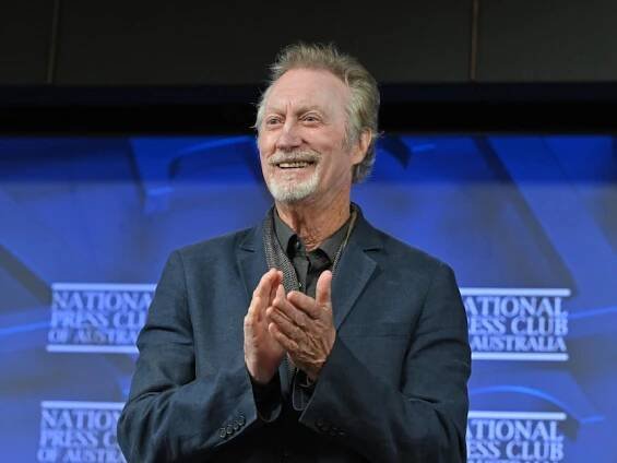 Bryan Brown smiling and clapping with a blue background, wearing a dark shirt, National Press Club of Australia written behind