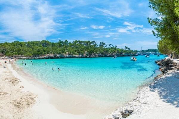Türkisblaue Bucht mit weißem Sandstrand und wenigen Badegästen und Kleinbooten, umrahmt von Bäumen -  Turquoise bay with a white sandy beach, few bathers and small boats, surrounded by trees © Serenity-H/stock.adobe.com