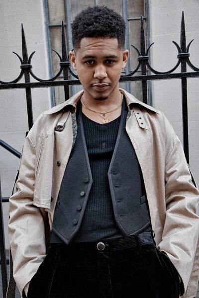person wearing a layered outfit with a decorative fence in the background