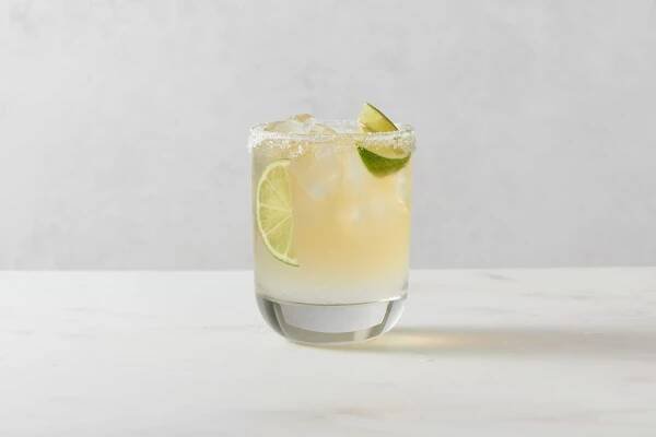 A beer margarita in a salt-rimmed cocktail glass, served with lime wedges