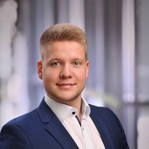 Ein Mann in einem blauen Anzug und einem weißen Hemd lächelt in die Kamera