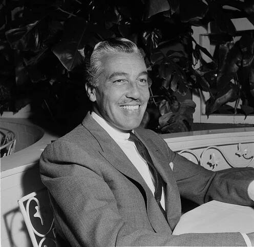 Cesar Romero sitting in a chair, smiling.