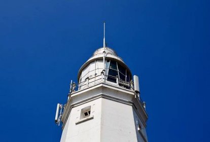 photograph of the top of a white lighthouse against a bright blue sky