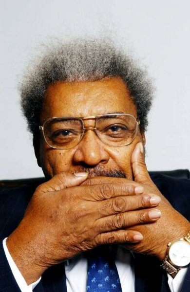 Portrait of person in suit and glasses with hand covering mouth.