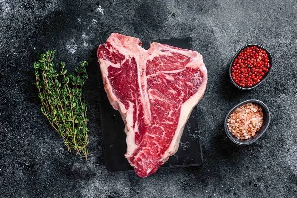Dry-aged Raw T-bone or porterhouse beef meat Steak with herbs and salt. Black background. Top view