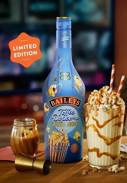 Baileys Toffee Popcorn bottle with two caramel-drizzled milkshakes topped with whipped cream and popcorn, set for a cosy movie night scene.