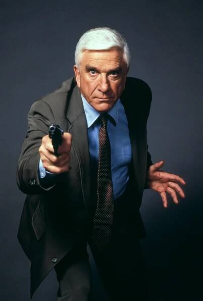 Leslie Nielsen pointing a gun in a suit.