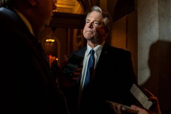 Senator Roger Marshall with a camera light shining on his face. Reporters surround him holding cellphones and recorders toward him.