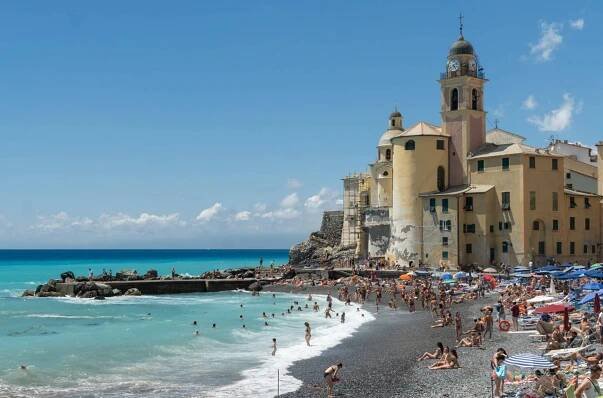 A big yellow church perched on a gray pebbly beach in Italy.