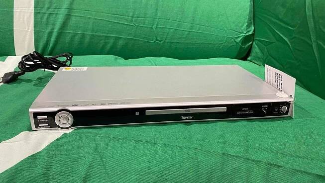 Ein getesteter DVD-Player von vorne auf einer grünen Couch liegend.