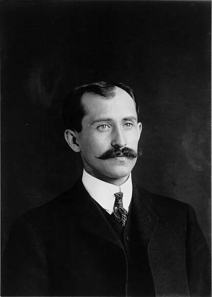 This is a photographic portrait of Orvile Wright, the younger of the two famed Wright brothers. He has a handlebar mustache and wears a suit and tie.
