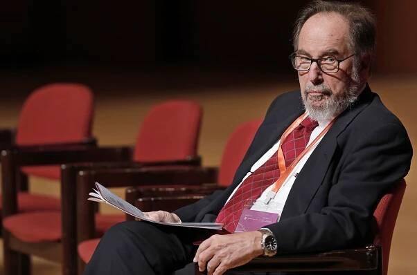 David Baltimore sitting in a chair holding papers