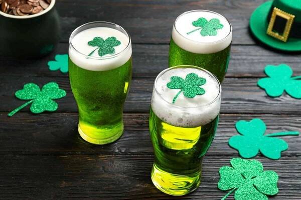 Green beer and clover leaves on black wooden table.
