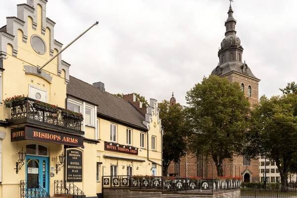 The yellow facade of the Hotel Bishops Arms with church behind and outdoor dining in front