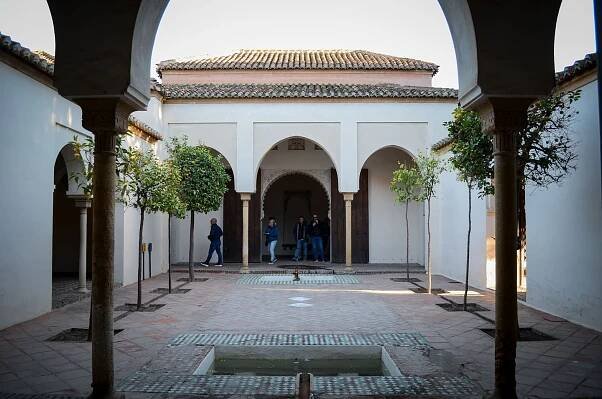 An interior courtyard of the Alcazaba in Malaga shows arched doorways, tiled floors, and small trees planted around a central fountain. A few visitors walk through the historic space. This image highlights the Alcazaba as a cultural landmark worth visiting on a solo trip to Malaga.