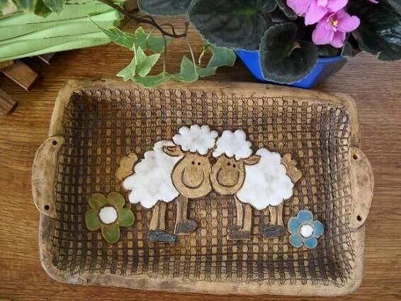 a tray with two sheep on it next to a potted plant and some flowers
