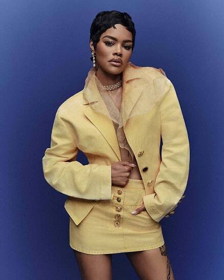 Teyana Taylor posing in a yellow outfit against a blue background