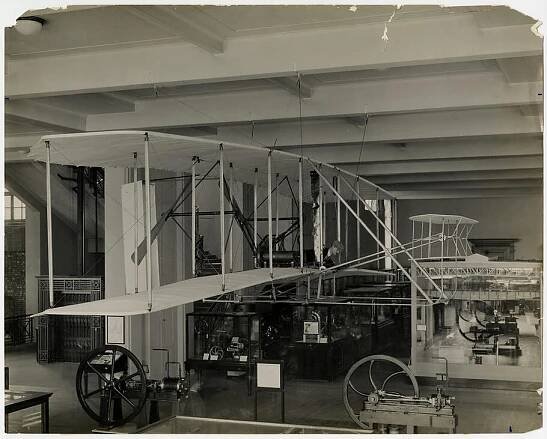 The Wright Flyer on display in an exhibit with other pieces of technology.