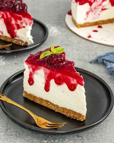 a slice of no bake cheesecake topped with cherry pie filling on a black plate.