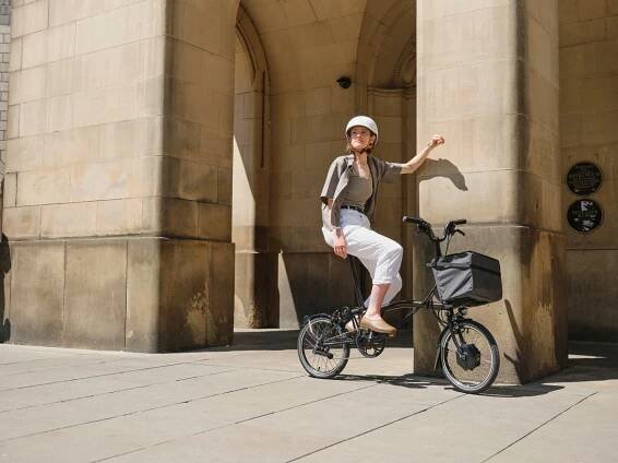 A woman riding a Flame Lacquer Brompton folding bike through the streets of Manchester