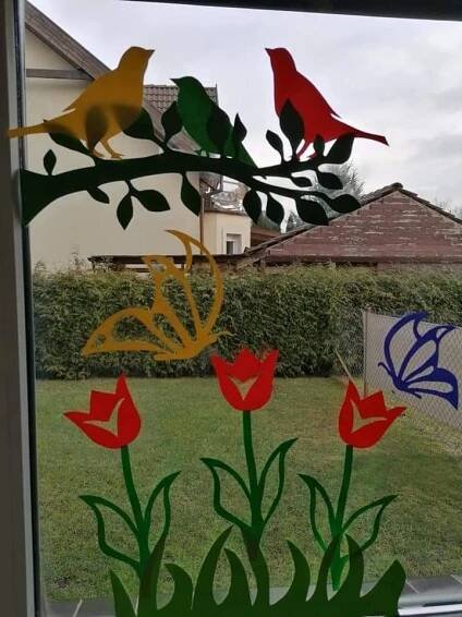 some birds are sitting on a tree branch in the window sill, with red and yellow flowers