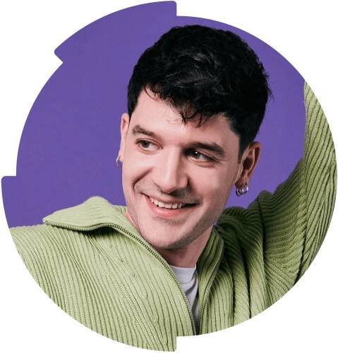 A smiling man with short dark hair, wearing a light green sweater, glancing to the side. He is posed against a circular purple background