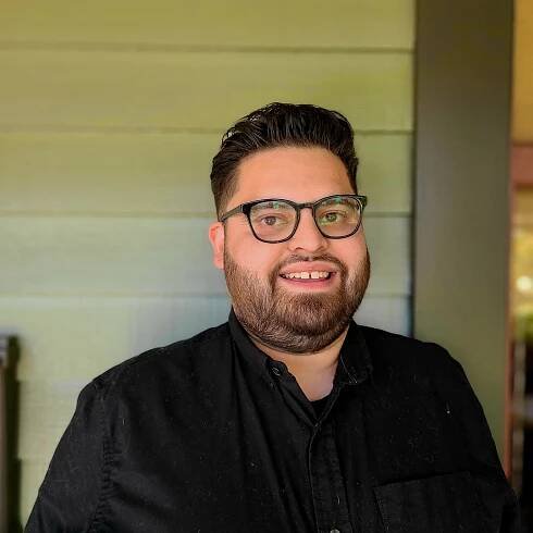 Headshot of a smiling Daniel Martinez wearing a black shirt, jacket and sunglasses