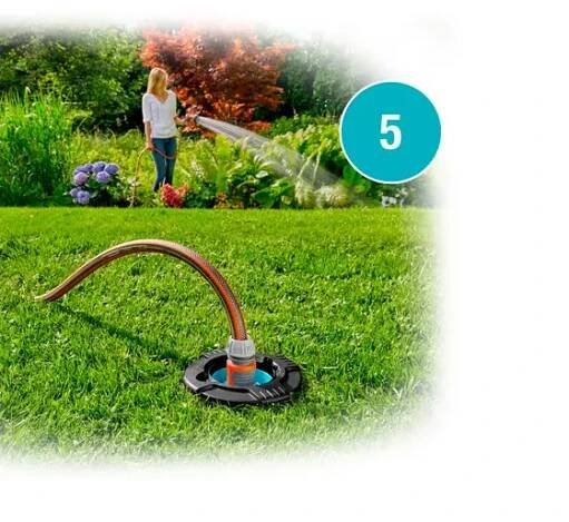 A woman waters her garden with a hose, alongside a sprinkler system set up on lush green grass. Vibrant flowers and foliage surround her. The borders of the image are blurred and a blue circle indicating step 5 is on it.