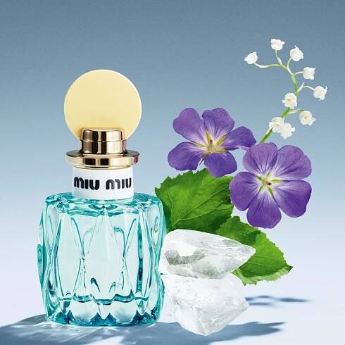 Tyrkysový flakón parfému Miu Miu s květinovým aroma, doplněný o fialové květy a kostky ledu, evokuje svěžest a eleganci.