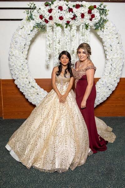 An elegant celebration under a white floral arch decorated with red roses and cascading white flowers.