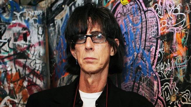 Ric Ocasek posing in front of graffitied wall
