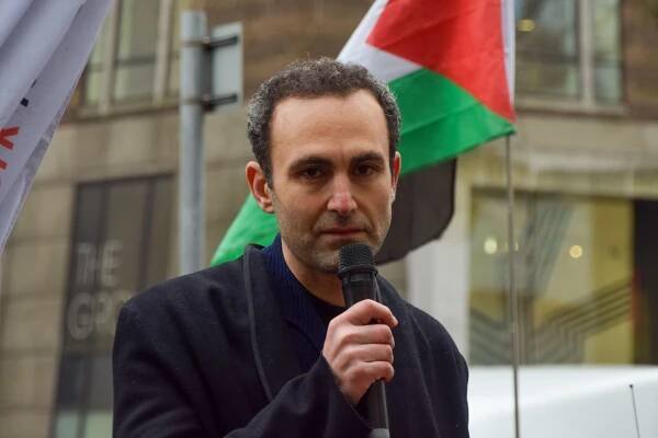 Khalid Abdalla speaking into a microphone at a protest.