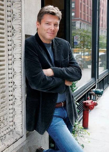 He was photographed standing with his  arms folded and leaning against a stone building on a city street, with a storefront window behind him. 