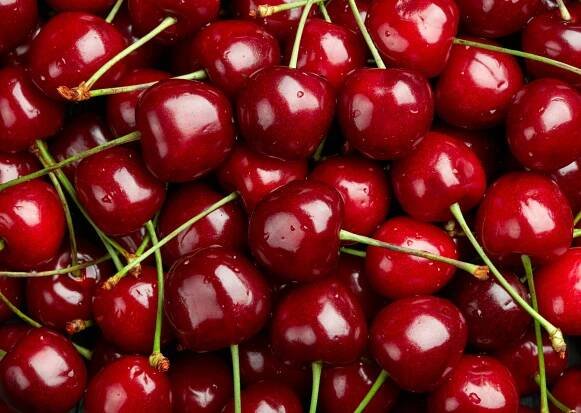 Eine Vielzahl frischer, saftiger Kirschen mit glänzender, roter Haut und grünen Stielen, die aufeinanderliegen. Diese Kirschen sind perfekt für Desserts, Smoothies oder als gesunder Snack.