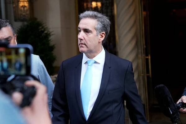 Michael Cohen in a dark suit and cerulean tie walks outside an apartment building. 