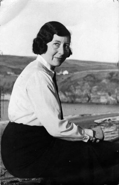 Black and white portrait of a sitting woman with short black hair with ocean and coastline behind her.