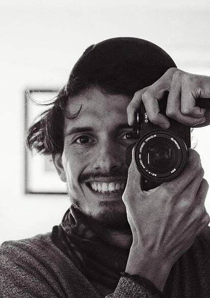 A black and white photo of a person holding a camera up near their face to take a photo while smiling