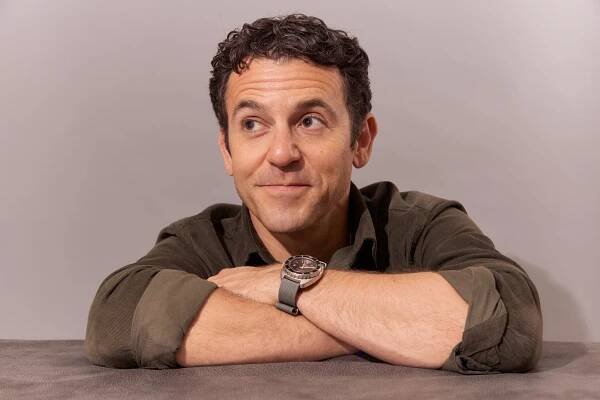 A portrait of Fred Savage with his arms crossed and resting on a shelf.