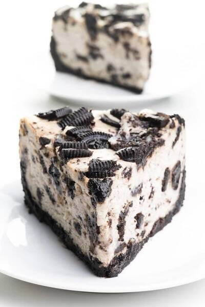 A slice of vegan Oreo cheesecake sits on a plate. Another slice is behind it.
