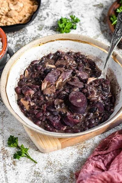 Bowl of feijoada in a bowl with a spoon resting in it. 