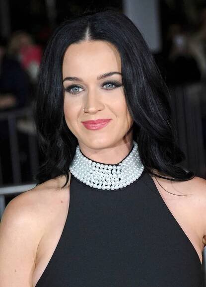 Katy Perry with long, black, middle-parted hair while wearing a black turtleneck dress  with pearls