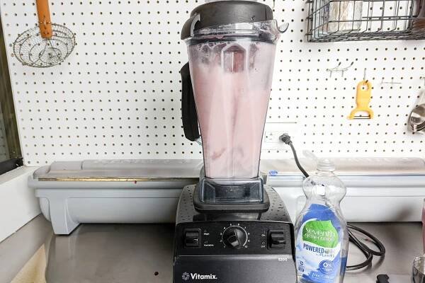 The Vitamix 5200 blending a light pink drink mixture on a stainless steel kitchen countertop.